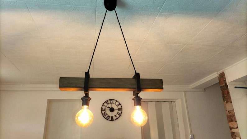 May include: A rustic wooden ceiling light fixture with two exposed bulbs hanging from black cords. The fixture is suspended from the ceiling with black metal brackets.