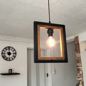 May include: A black framed pendant light with a wood accent and a single light bulb. The light is hanging from a black cord.
