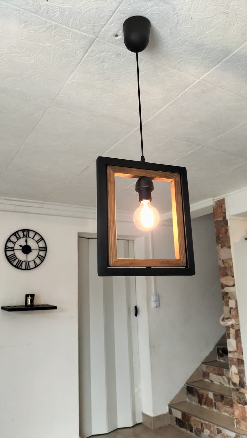 May include: A black framed pendant light with a wood accent and a single light bulb. The light is hanging from a black cord.
