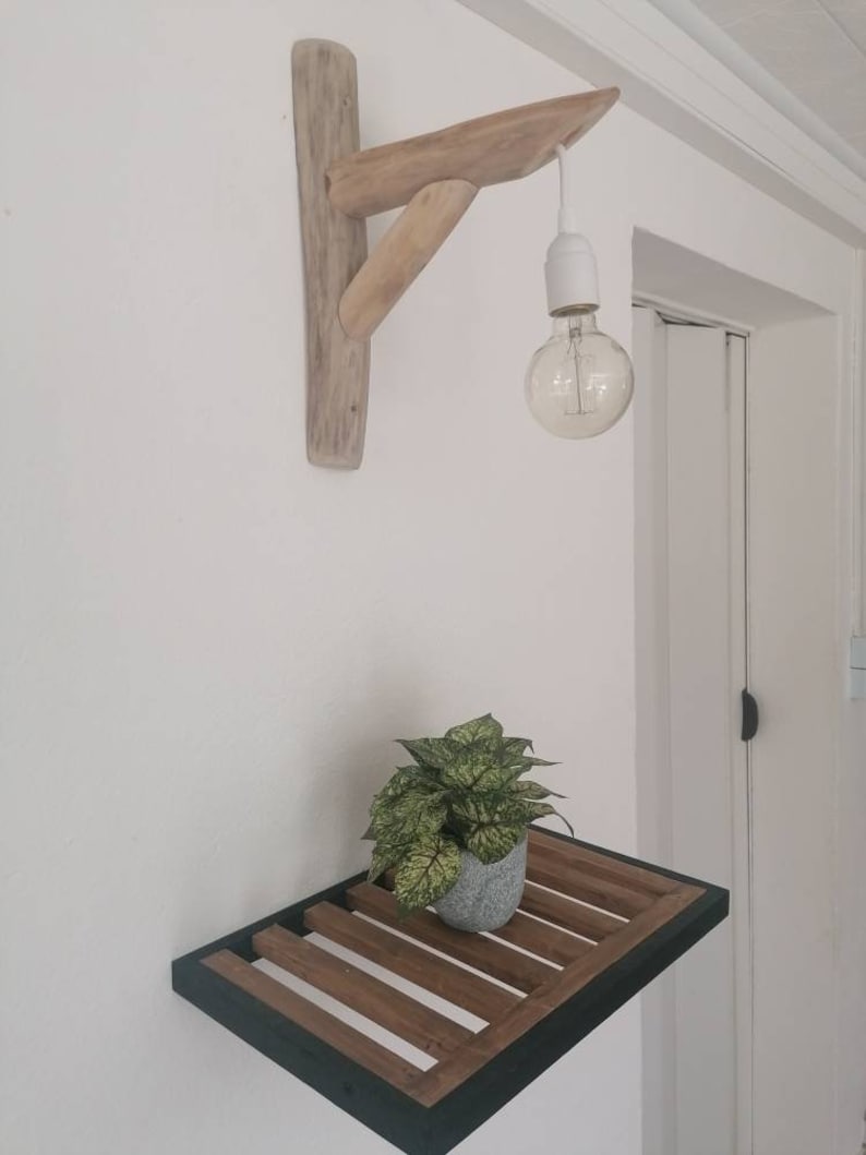 May include: A wooden shelf with a black metal frame and a small potted plant. A wooden light fixture with a hanging light bulb is mounted on the wall above the shelf.