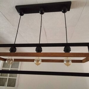 May include: A rectangular black metal frame with a wooden beam across the top and bottom. Four light bulbs hang from the frame, each with a black metal cap.