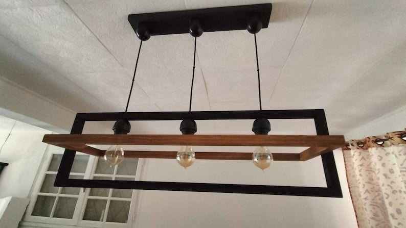 May include: A rectangular black metal frame with a wooden beam across the top and bottom. Four light bulbs hang from the frame, each with a black metal cap.