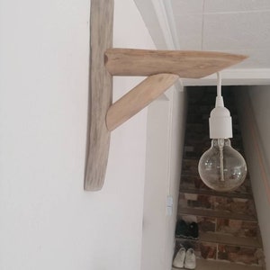 May include: A wooden wall shelf made from driftwood with a light bulb hanging from it. The shelf is mounted on a white wall and the light bulb is hanging over a set of stairs.