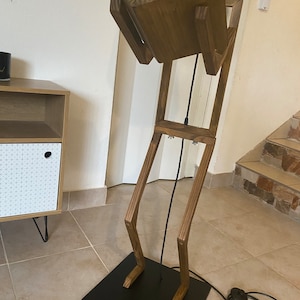 May include: A wooden floor lamp with a black shade and a wooden base shaped like a person. The lamp has a black cord and a black plug.
