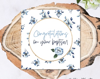 May include: A white card with a blue floral pattern and gold circle. The text inside the circle reads "Congratulations on your baptism".