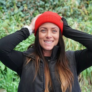 May include: A woman wearing a black puffer vest with a red beanie and a black long-sleeved shirt.