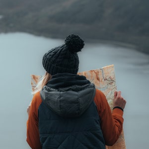 Peut inclure: Une personne portant un bonnet noir avec un pompon et une veste matelass&eacute;e bleu fonc&eacute; avec une manche orange regarde une carte.