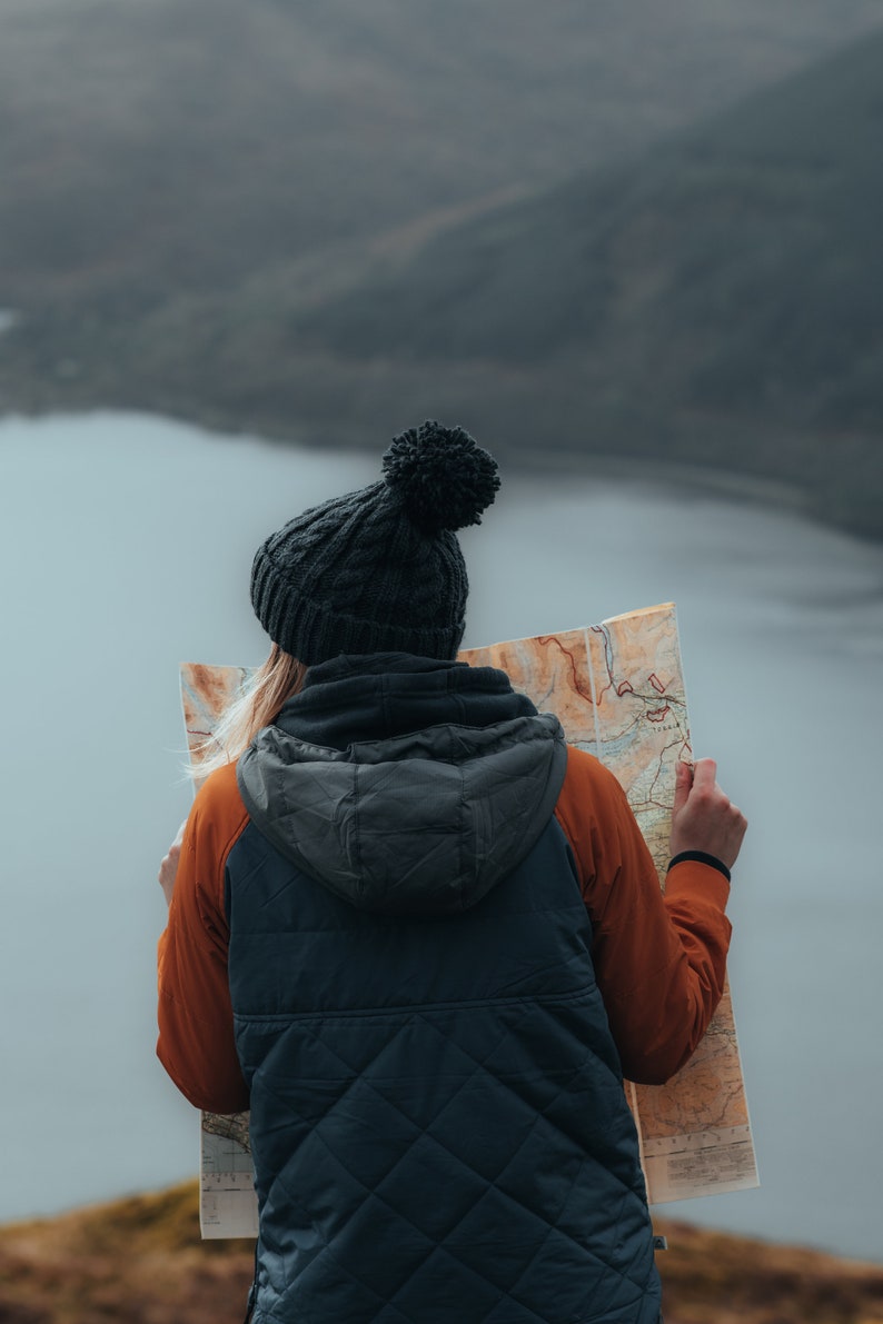 Peut inclure: Une personne portant un bonnet noir avec un pompon et une veste matelass&eacute;e bleu fonc&eacute; avec une manche orange regarde une carte.