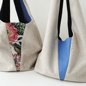 Pode incluir: Duas bolsas tote grandes feitas de tecido de linho natural. Uma bolsa tem um painel de estampa floral e um painel de denim azul. A outra bolsa tem um painel de denim azul sólido.