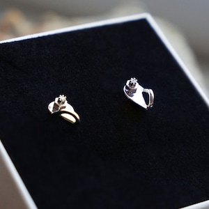 Könnte beinhalten: Ein Paar silberne Ohrringe mit einem kleinen, klaren Stein in der Mitte jedes Ohrrings. Die Ohrringe befinden sich in einer weißen Schachtel mit schwarzem Innenraum.