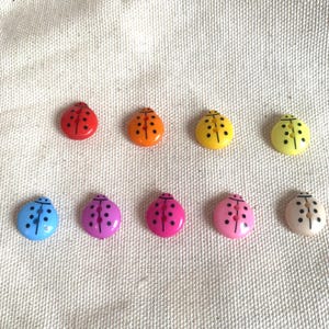 May include: Ten ladybird-shaped buttons in a variety of colours: red, orange, yellow, green, blue, purple, pink, and off-white. Each button has black dot details and two holes for sewing.