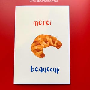Bonita tarjeta de regalo tamaño A5 con un croissant de agradecimiento con la frase "merci beaucoup" dibujada a mano