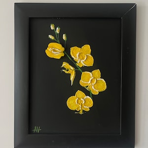 May include: A framed painting of yellow orchids on a black background. The flowers are textured and have white accents. The painting is in a black frame and signed in the lower left corner.