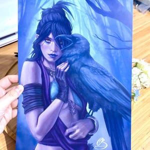 Peut inclure: Une femme aux cheveux bleus et à la robe violette tient un corbeau bleu dans ses bras. L'arrière-plan est une forêt bleue et blanche.
