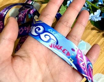 May include: A blue and purple lanyard with white clouds and the word "Jinxed" printed on it.