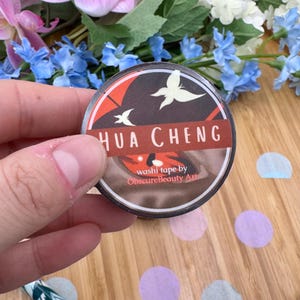 May include: A roll of washi tape with a brown and red background featuring a white butterfly and the text "HUA CHENG" in white. The text "washi tape by ObscureBeautyArt" is printed in white on a red background.