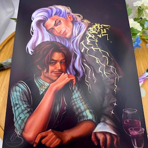 May include: A print depicting two figures, one with long, lavender hair and the other with brown hair, in a romantic pose. The artwork has a dark background with gold accents on the clothing. Two glasses of red wine are visible.