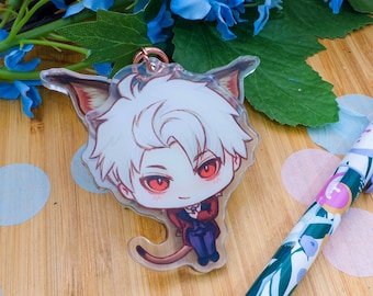 May include: A clear acrylic keychain featuring a cartoon character with white hair, red eyes, and a red and blue outfit. The keychain has a copper-colored ring. A pen with a floral design and blue flowers are also in the image.