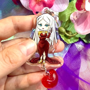 May include: A clear acrylic keychain featuring a stylized illustration of a character with long white hair, wearing a dark red gown with gold accents, holding a small glass. A translucent red heart-shaped charm hangs from the bottom of the keychain.