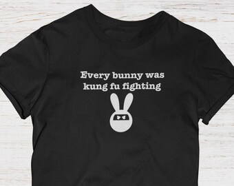 May include: Black t-shirt with the text "Every bunny was kung fu fighting" in white, above a white bunny graphic wearing a ninja mask. The shirt has short sleeves and a crew neck.