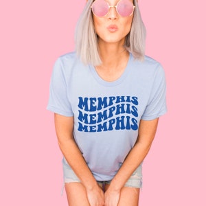 May include: A light blue t-shirt with a blue graphic that says "MEMPHIS" three times in a retro font.