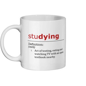 May include: White ceramic mug with a black and red design. The mug features the word "studying" in red and a definition of the word as "Act of texting, eating and watching TV with an open textbook nearby."