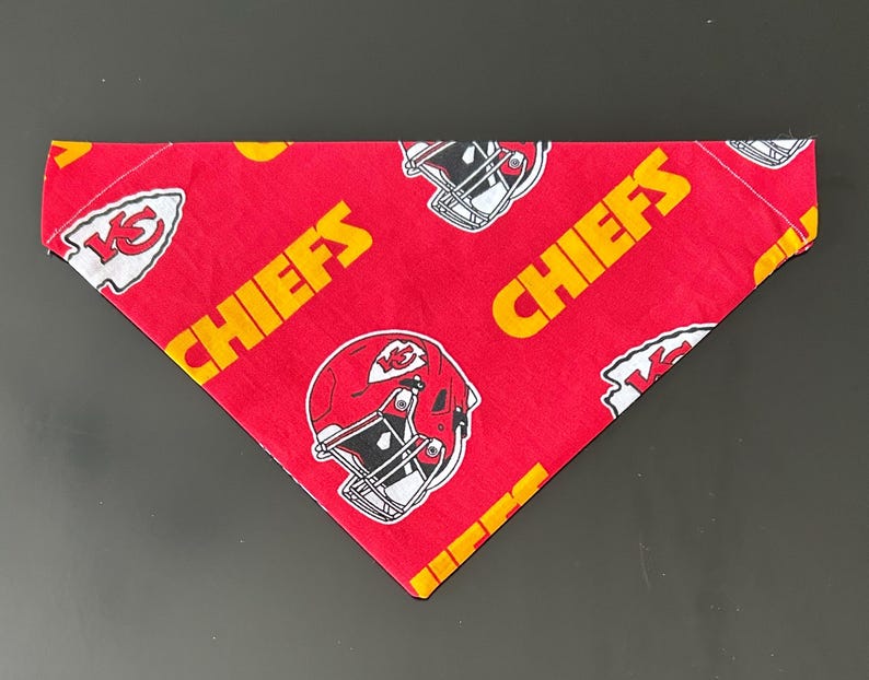 May include: Red and yellow Chiefs bandana with a repeating pattern of football helmets and the word "CHIEFS". The bandana is triangular in shape and has a white border.