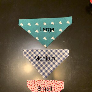 May include: Three triangular pet bandanas in different sizes. The large bandana is teal with white tree patterns. The medium bandana is blue and white checkered. The small bandana is red with pink heart patterns.