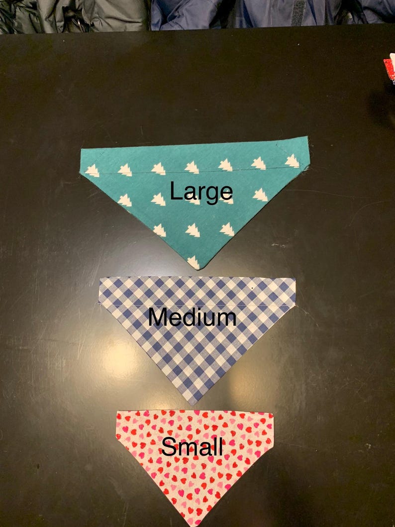 May include: Three triangular pet bandanas in different sizes. The large bandana is teal with white tree patterns. The medium bandana is blue and white checkered. The small bandana is red with pink heart patterns.