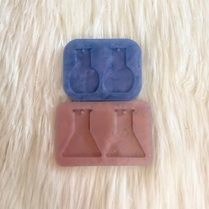 May include: Two silicone moulds for making earrings. The top mould is blue and has two round shapes with a small hole at the top. The bottom mould is pink and has two flask shapes with a small hole at the top.