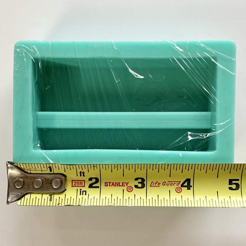 May include: A turquoise silicone mold with two rectangular cavities. The mold is approximately 3 inches long.