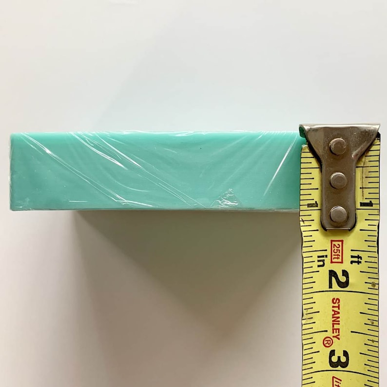 May include: A turquoise blue rectangular block wrapped in clear plastic is measured with a yellow tape measure. The tape measure reads 2 inches and 3 feet.