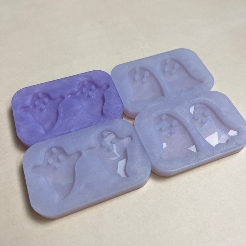 May include: A set of four silicone molds for making ghost-shaped resin crafts. The molds are translucent purple and have a smooth, shiny finish.