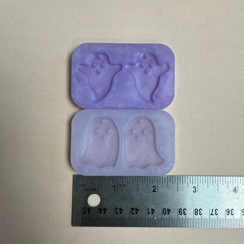 May include: Two purple silicone molds for making ghost-shaped resin crafts. Each mold has two cavities, and the molds are approximately 1 inch wide.