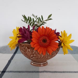 May include: A brown ceramic vase with a horse design, filled with yellow, orange, and purple flowers.