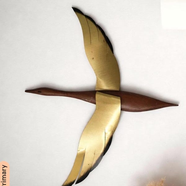 Peut inclure: Une sculpture murale d'oiseau composée d'un corps en bois brun foncé et de deux grandes ailes en métal doré. Les ailes sont positionnées dans un mouvement de vol ascendant et descendant, avec des accents noirs aux extrémités des plumes. L'oiseau est représenté dans une pose de vol horizontale avec un bec pointu et une queue effilée.