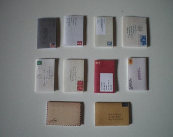 May include: A collection of nine envelopes in various colors and sizes, including white, red, brown, and gray. Some envelopes have stamps and handwritten addresses.