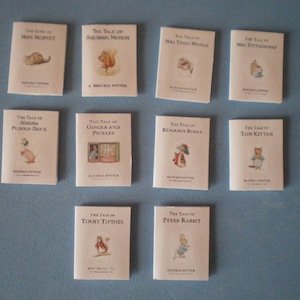 Op de afbeelding: Een verzameling van tien miniatuurboeken met de klassieke kinderverhalen van Beatrix Potter. De boeken zijn gerangschikt in twee rijen van vijf, met de titels zichtbaar op elke omslag. De boeken zijn allemaal wit met zwarte tekst en illustraties.