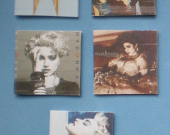 May include: Four different Madonna album covers. The first cover is light blue with gold accents and the title "Immaculate" and "Madonna" in gold lettering. The second cover is a close-up of Madonna with her hair styled in a blonde, curly, and teased style. The third cover is a close-up of Madonna with her hair styled in a blonde, curly, and teased style. The fourth cover is a close-up of Madonna with her hair styled in a blonde, curly, and teased style.