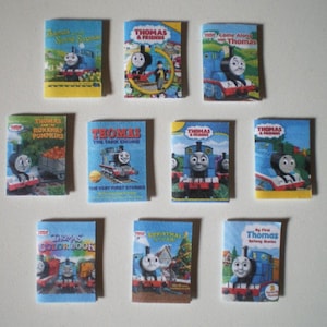 May include: A collection of ten miniature Thomas the Tank Engine books. The books feature various covers with Thomas and his friends, including "Thomas & Friends", "Come Along Thomas", "Thomas and the Runaway Pumpkins", "Thomas the Tank Engine", "Thomas & Friends", "Thomas & Friends", "Thomas Colour Book", "Christmas Train", and "My First Thomas".