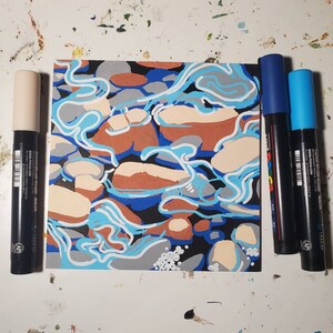 May include: A close-up of a small abstract painting with a blue, white, and brown color scheme. The painting depicts a swirling pattern of water and rocks. Three markers are visible in the background.