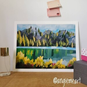 May include: A painting of a lake surrounded by trees with a reflection of the trees in the water. The painting is framed and has a white mount. The title of the painting is "The Eye" and the artist's signature is in the bottom right corner.