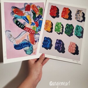May include: Two paintings of gummy candies. The first painting shows a pile of colorful gummy worms on a pink background. The second painting shows a grid of nine gummy bears in different colors, including red, orange, yellow, green, blue, and purple.