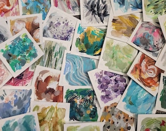 Puede incluir: Una colección de pequeñas pinturas abstractas de acuarela sobre papel blanco. Las pinturas presentan una variedad de colores y texturas, incluyendo azul, verde, morado, naranja y amarillo.
