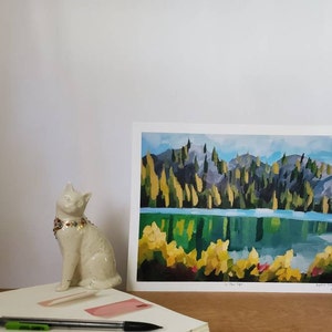 May include: A painting depicting a lake scene with a mountain range in the background. The lake is a bright blue and the mountains are a dark green. The trees are a mix of green and yellow. The painting is signed by the artist and dated 2021.