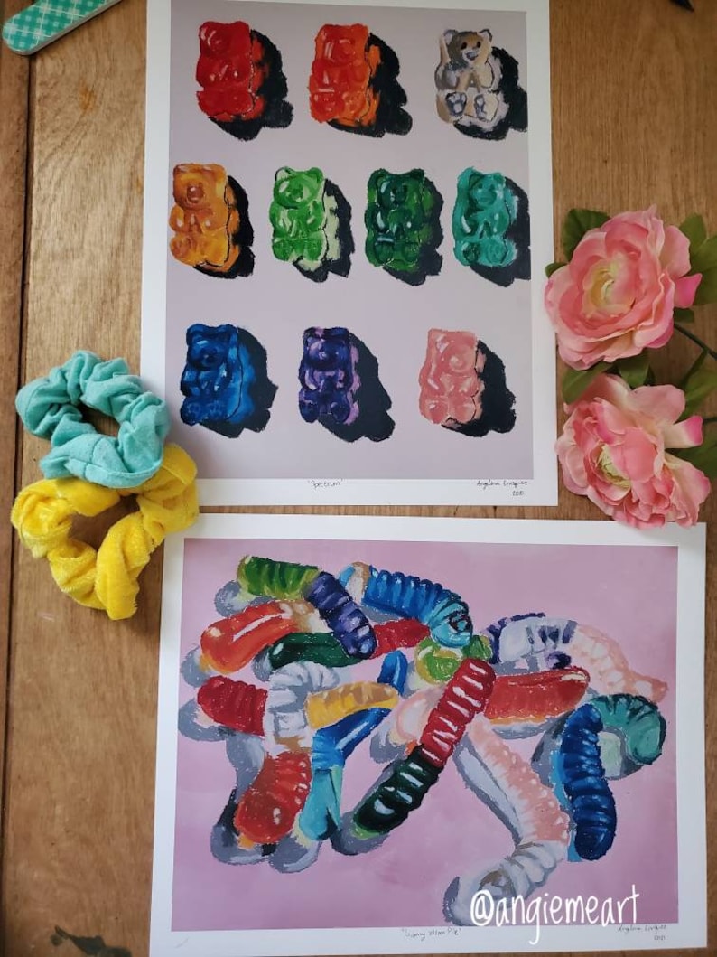 May include: Two prints of gummy candy paintings. The first print features a grid of 12 gummy bears in various colors, including red, orange, yellow, green, blue, and purple. The second print features a pile of gummy worms in various colors, including red, orange, yellow, green, blue, and purple. The prints are on a white background with a pink background.