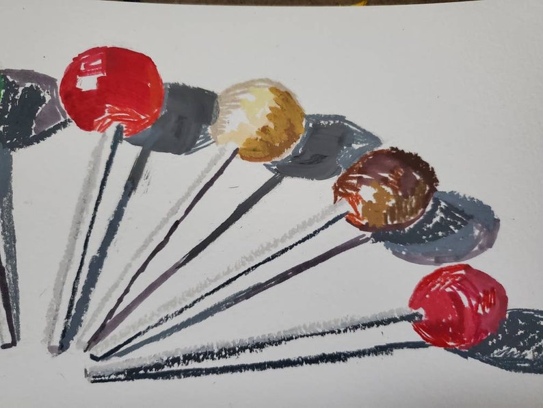 May include: A collection of seven colorful lollipops with gray sticks arranged in a fan shape on a white background.