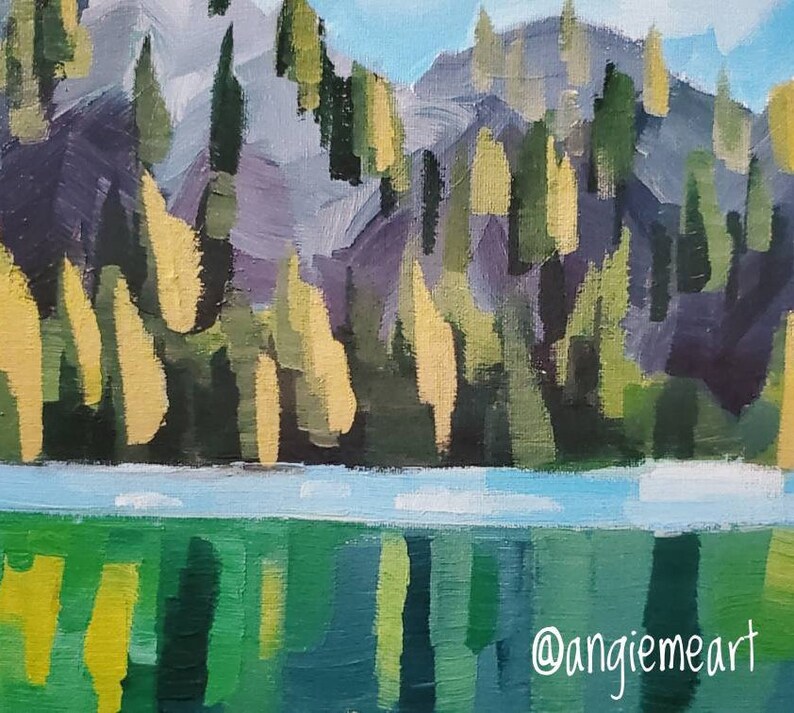 May include: A painting depicting a mountainous landscape with a lake in the foreground. The mountain is rendered in shades of purple, green, and yellow, with a blue sky above. The lake is a bright blue with green reflections. The artist's signature, "@angiemeart", is in the bottom right corner.