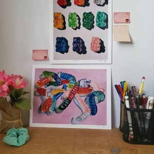 May include: Two framed prints of gummy bear paintings. The top print features a grid of nine gummy bears in different colors. The bottom print features a pile of gummy worms in various colors and shapes.