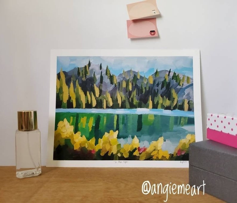 May include: A painting of a lake surrounded by trees with a reflection of the trees in the water. The painting is framed and has a white mount. The title of the painting is "The Eye" and the artist's signature is in the bottom right corner.